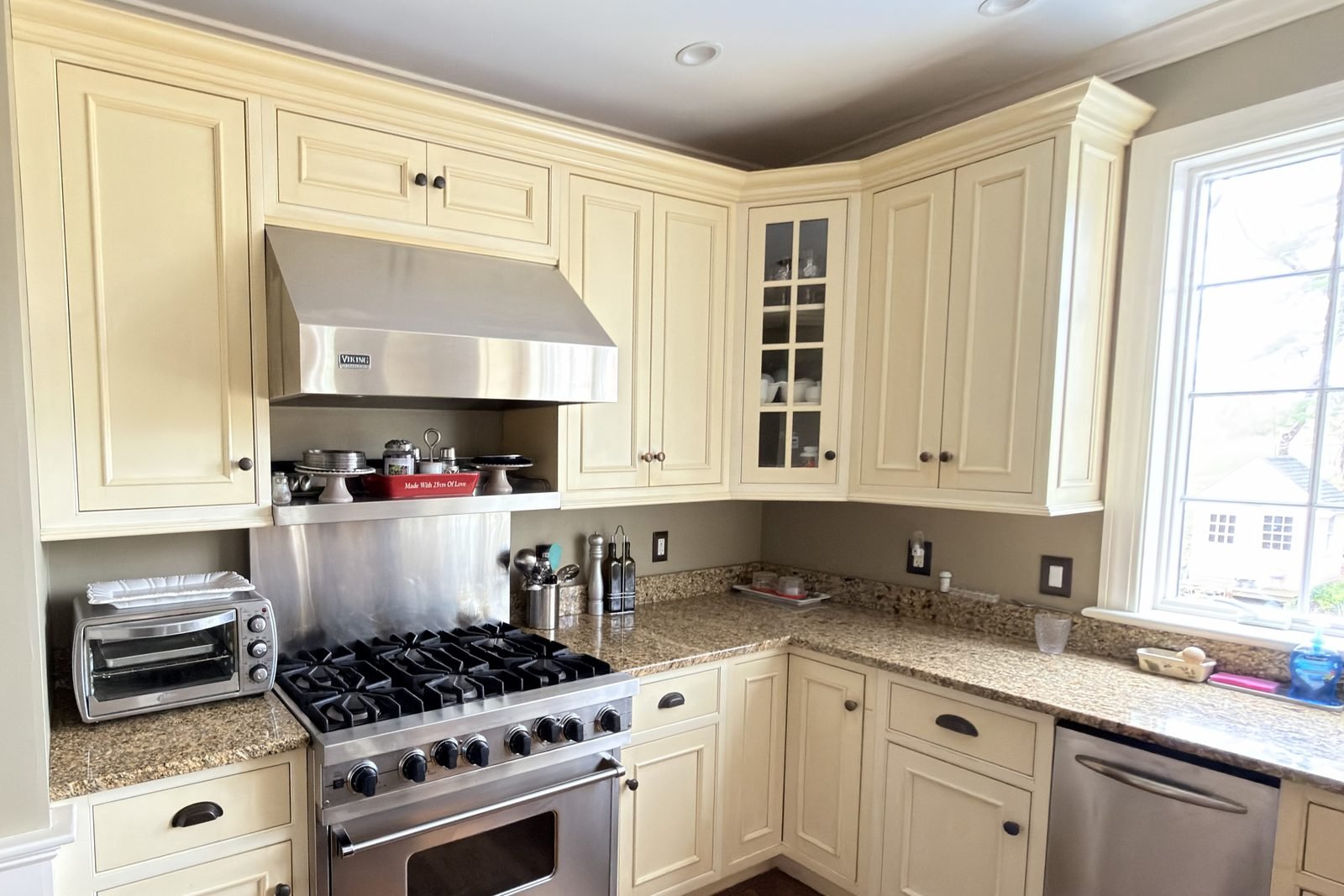 The same kitchen range wall with dated yellowed cabinets before refinishing