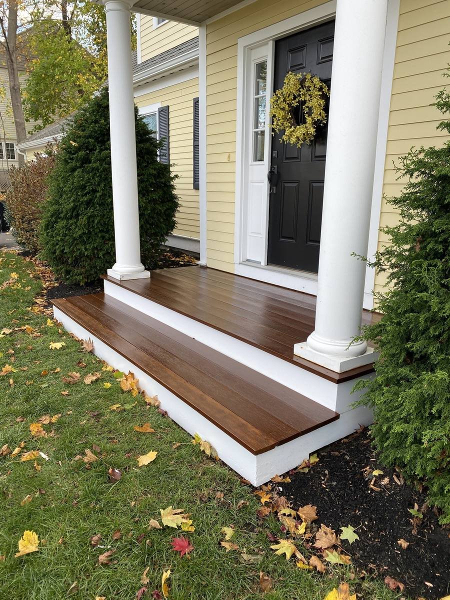 Front entry with white painted columns, a black door and a freshly stained porch deck